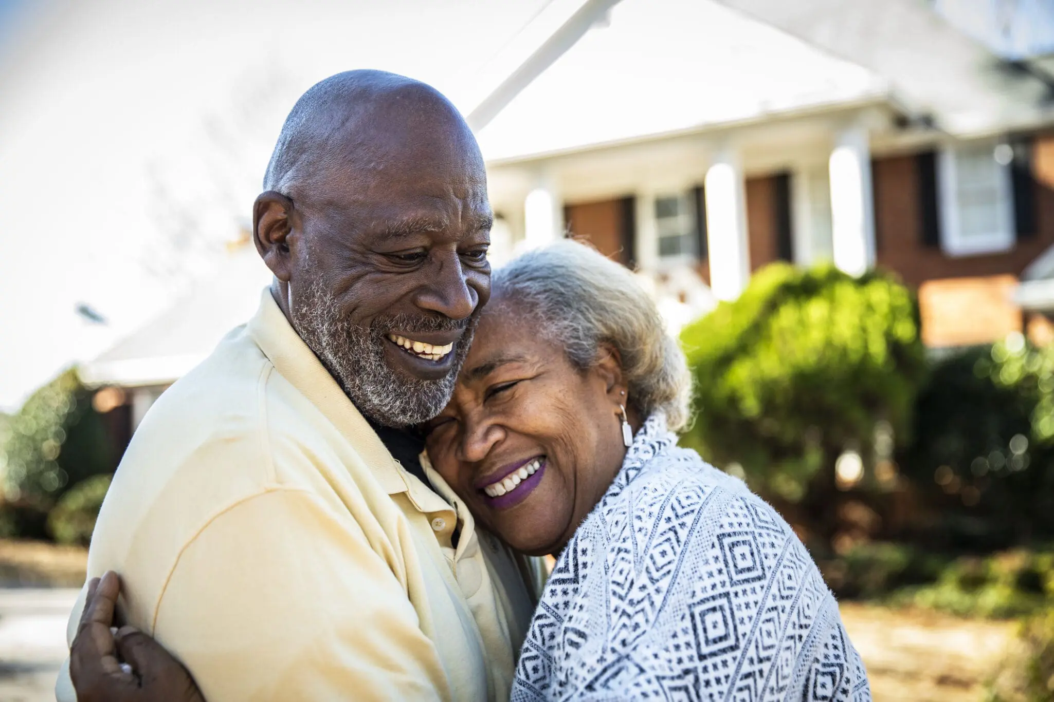 Senior couple embracing in front of residential home A smiling senior couple embracing.