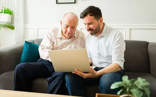 senior man looking at paper with son on couch