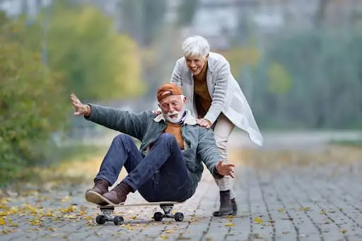 Senior couple pushing on skateboard outside