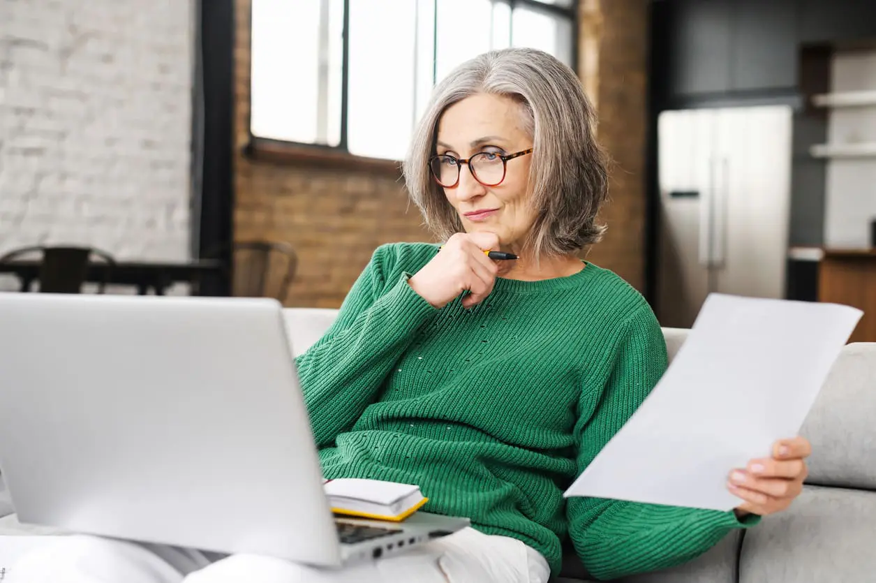 Serious senior accountant sitting on the living room and looking at the laptop Senior woman post-retirement planning.