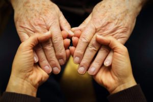 A close up photo of two seniors holding hands