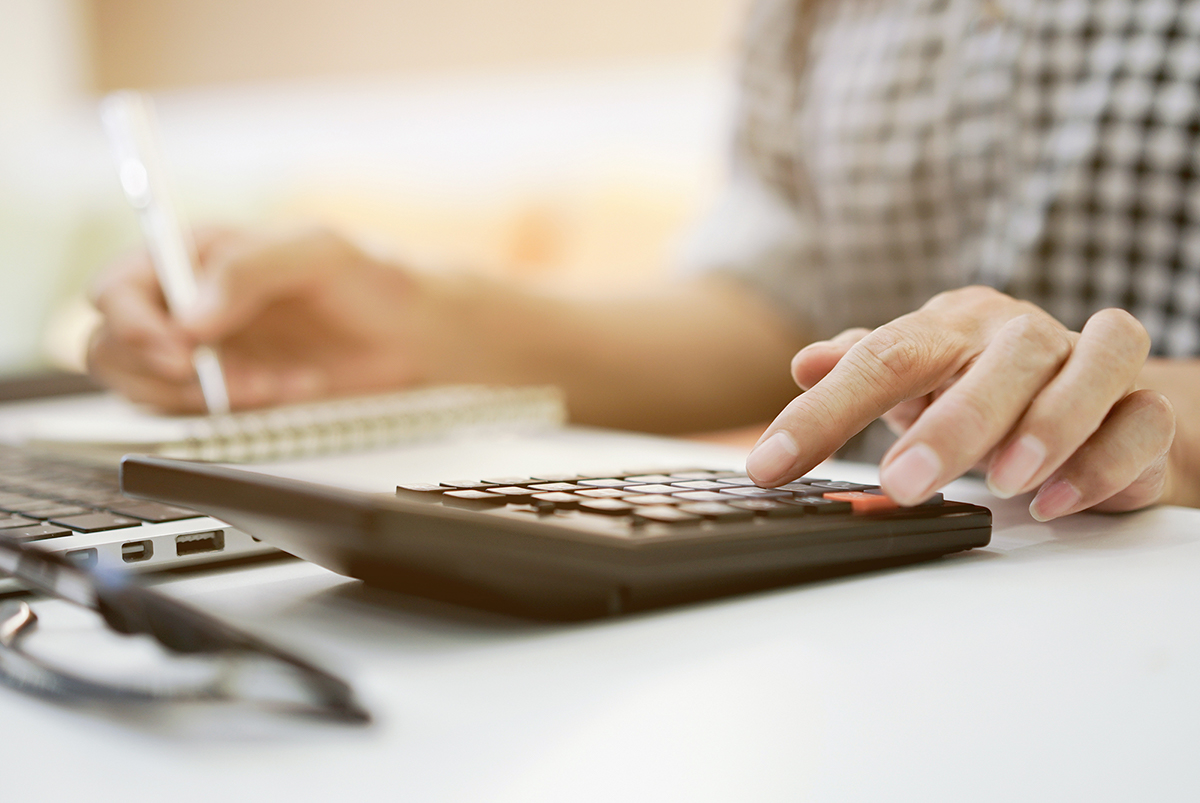 A senior woman takes notes while using a calculator