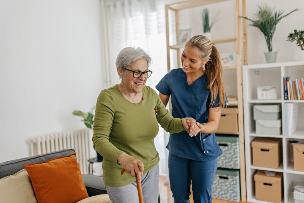 Female caregiver helping and supporting senior patient to walk at home, senior woman in lifecare is standing and holding walking cane